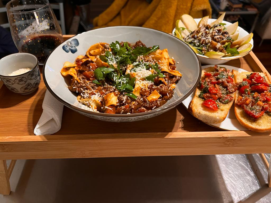 A surprise dinner served on a wooden tray: pappardelle, bruschetta and a glass of red wine.