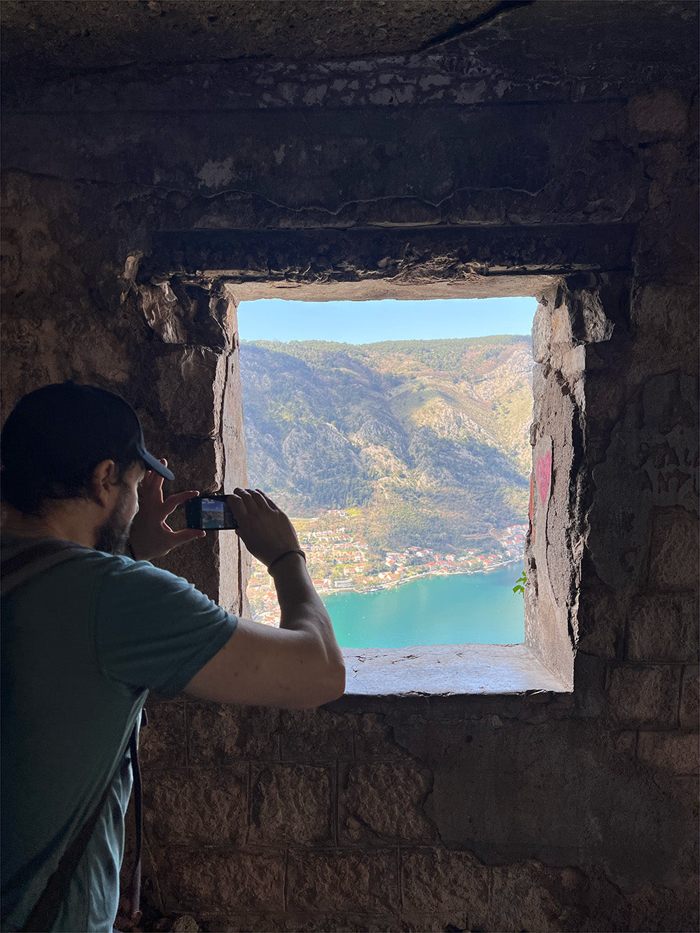 Demi photographing a bay and mountains through a square stone window.